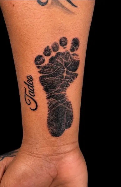 Baby footprint and name — Black & gray realism tattoo on wrist / forearm